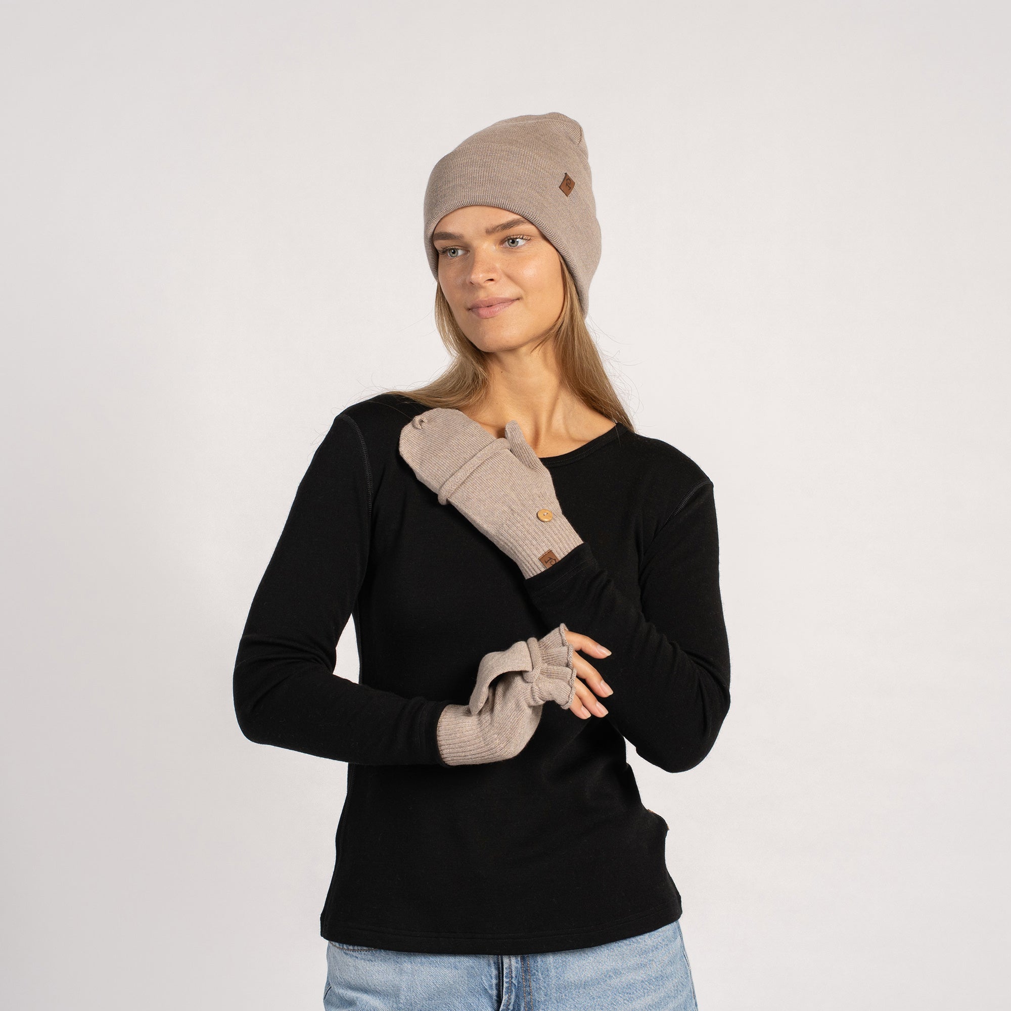 Frontal portrait of a woman smiling slightly while wearing a creamy-beige beanie and convertible mittens with flap button detail.