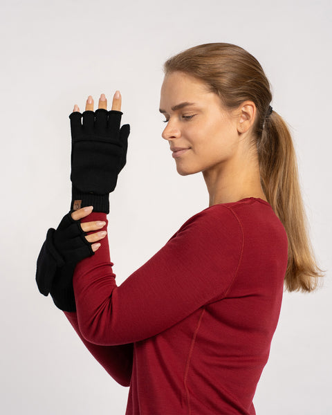 Mid-shot of a woman in a red top, arms crossed and showcasing black convertible mittens with the flap pulled back to reveal fingers.
