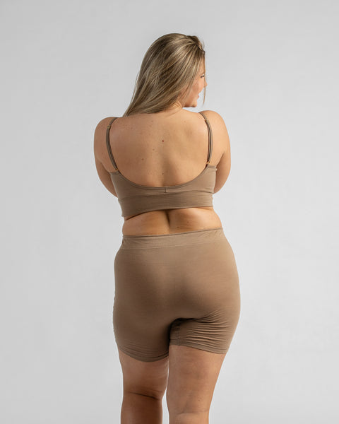 Back view of a model looking over her shoulder, wearing a beige sports bra with thin straps and matching beige biker shorts.