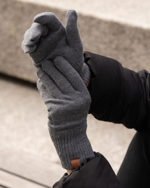 Person wearing dark gray Merino wool knit gloves, showing the glove fit and ribbed cuffs outdoors.