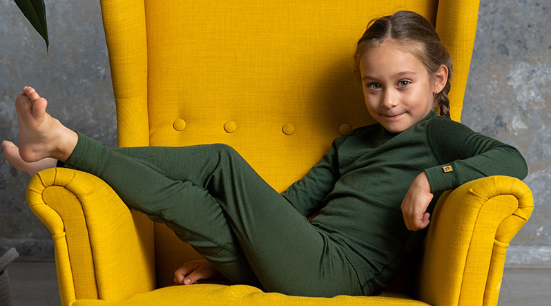 Little girl sitting on the chair and wearing green matching merino wool set