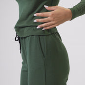 The model putting her hand inside the pockets and tying the waist of the menique women's sweatpants in dark green color. She is raising her legs in the video, to display that she can move freely.