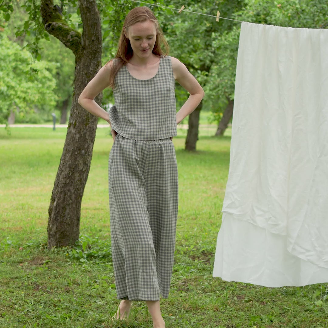 The model is slowly walking forward, towards the camera, wearing a matching set, featuring the ANA crop top and LANA culottes  in green gingham. She is smiling, with her hands raised or put on her hips.