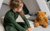 A girl sitting next to a plush bear, wearing a dark green merino wool base layer set.