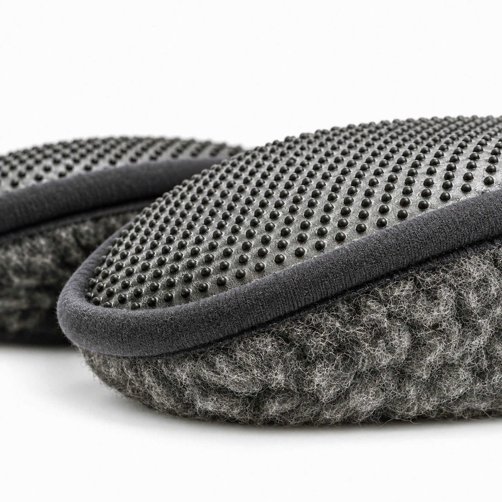 A top-down view of a pair of dark gray fuzzy slip-on slippers with textured gray insoles and a "MENIQUE" tag on the side of the left slipper.