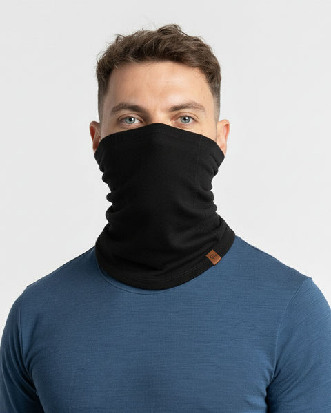 Man wearing a black merino wool neck gaiter with a blue base layer top against a light background.
