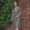 Young woman posing near the red brick wall, wearing stone green color linen tunic dress Joelle.