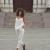 Beautiful woman posing in the city, wearing pure white linen slip top and pure white linen pants with black sandals.