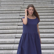 Young woman posing in a city street on stears wearing linen smock dress cecilia in a storm blue color.