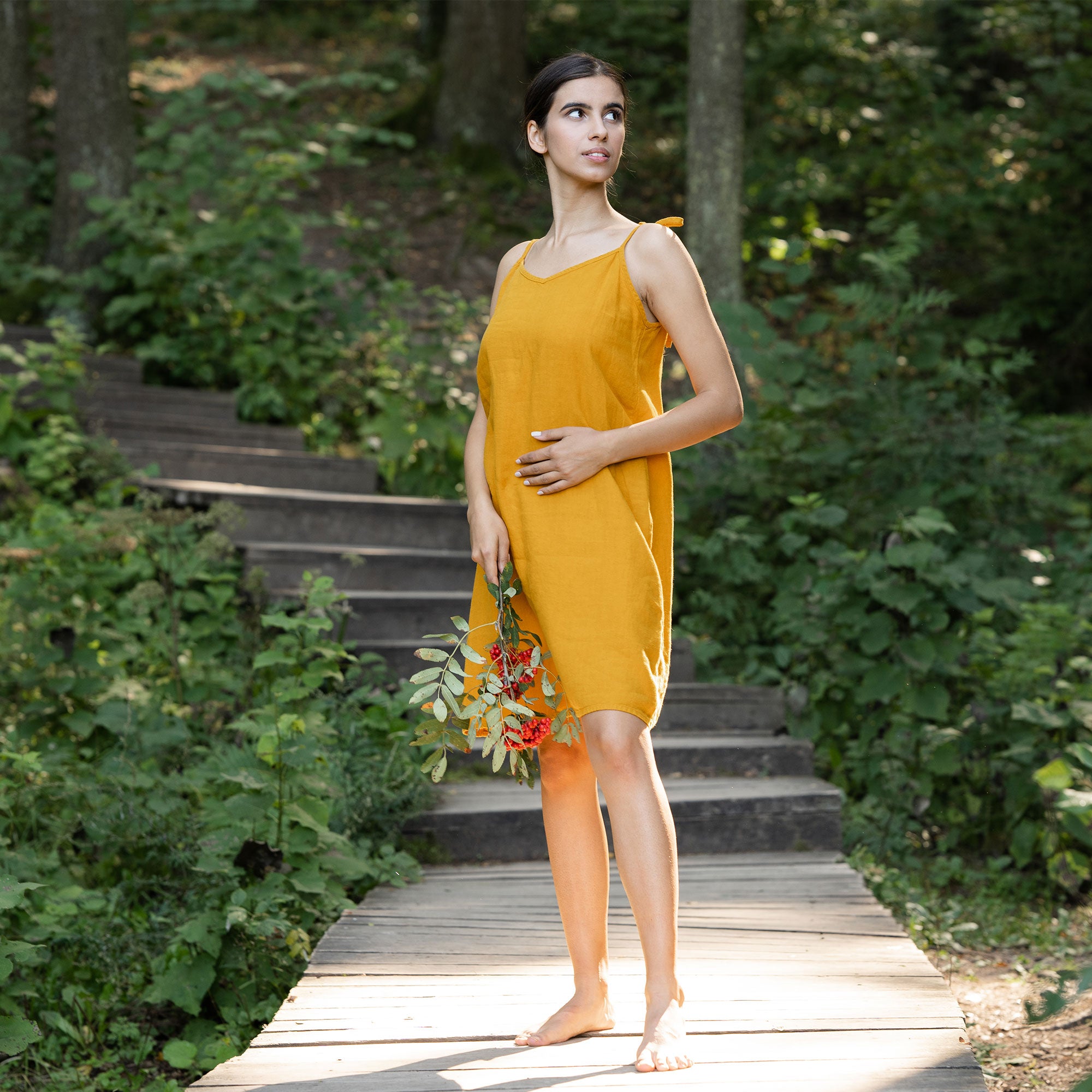 Woman wearing spicy yellow linen dress and standing in  the forest