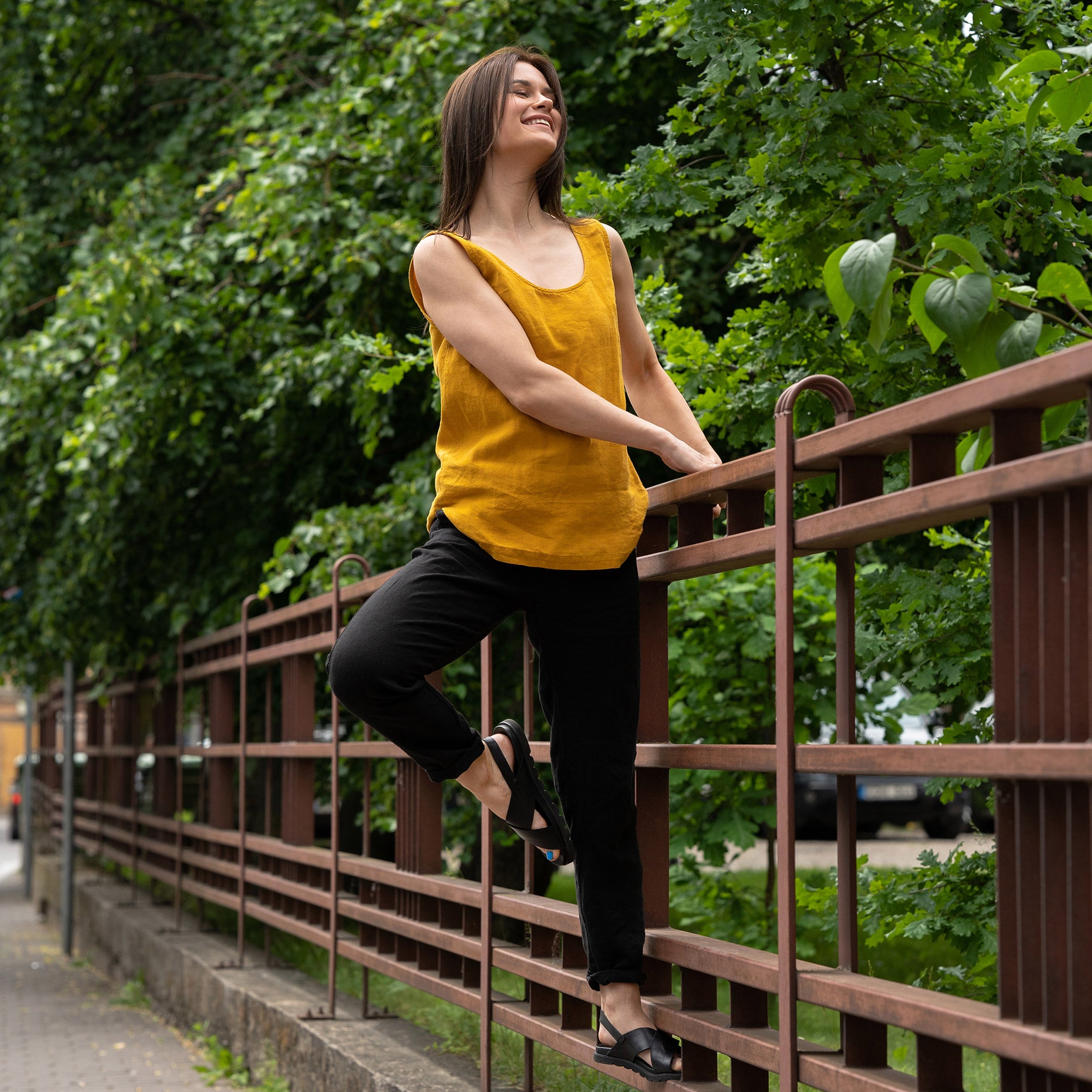 A young woman posing in a city street wearing linen set with a spicy yellow  tank top Hana and pure black linen pants Dakota.