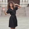 Woman outside in the city smiling and spinning around wearing a pure black linen dress Eliana.